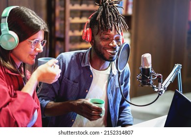 Multi-ethnic couple of young people talking using microphones with antipop to record a streaming live video podcast session online - 20s content creators having fun recording a vlog