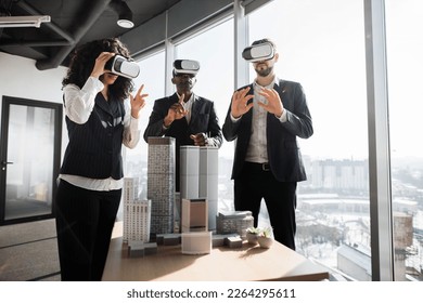 Multiethnic creative business team using virtual reality headsets at the meeting in modern office. Group of developers using virtual reality simulators, standing around table with 3d city model - Powered by Shutterstock