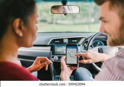 Multiethnic diverse lover couple using navigation system on smartphone in car. Mobile phone application, crowdsourced taxi or ride hailing app service, modern gadget or family travel lifestyle concept