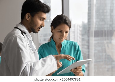 Multiethnic doctors engaged in collaborative medical consultation, discuss patient disease diagnose or treatment plan, reviewing information, focusing on tablet. Teamwork, modern tech in healthcare - Powered by Shutterstock