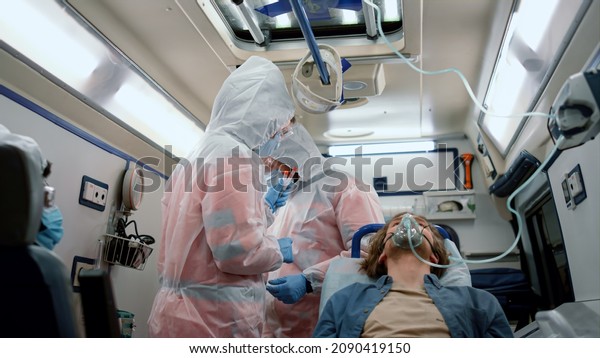 Multiethnic doctors holding samples of\
coronavirus test in emergency car. Paramedics in masks and\
protective suits working in mobile laboratory. Injured patient in\
oxygen mask transferring to\
hospital