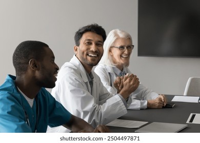 Multiethnic doctors laughing engaged in pleasant conversation seated at table in meeting room, lead discussion, share humorous or insightful comment, take part in group medical team meeting or seminar - Powered by Shutterstock