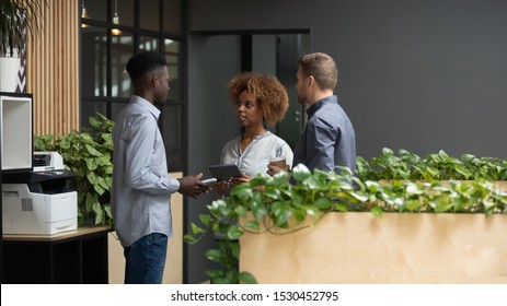 Multi-ethnic Employees Three Office Workers Standing In Modern Hallway Talking Planning Current Issues Having Informal Meet In Workplace Corridor, Cooperation And Friendly Relations At Work Concept