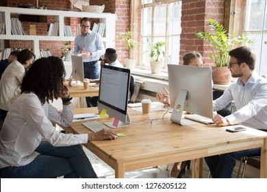Multi-ethnic employees working on computers in modern office room, corporate staff team people diverse workers group using desktop monitors sitting at desks in open shared coworking space together