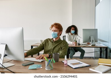 Multiethnic employees working on computers in office during Coronavirus epidemic. Business people sitting at desks and wearing medical masks. Collective and team work during Covid-19 pandemic