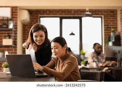 Multiethnic employees working together at office desk, reviewing financial data on laptop. An inclusive workspace where caucasian manager and asian wheelchair user discuss business growth strategies.