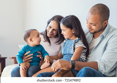 Multiethnic family playing with happy baby son at home. Parent and children relaxing together on the sofa at home in the living room. Little girl sitting on leg of dad looking her new cute brother. - Powered by Shutterstock