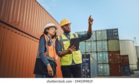 Multiethnic Female Industrial Engineer with Tablet and Black African American Male Supervisor in Hard Hats and Safety Vests Stand in Container Terminal. Colleagues Talk About Logistics Operations. - Powered by Shutterstock