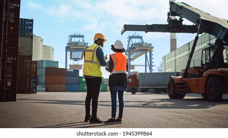 Multiethnic Female Industrial Engineer with Tablet and Black African American Male Supervisor in Hard Hats and Safety Vests Stand in Container Terminal. Colleagues Talk About Logistics Operations. - Powered by Shutterstock