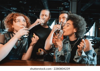 Multiethnic friends drinking tequila shots and holding fresh lime in bar - Powered by Shutterstock