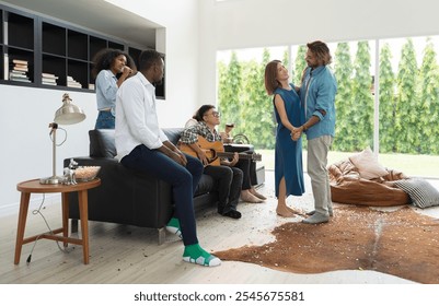 Multiethnic friends gathering in modern living space and celebrating party with music and dance. Couple dancing while others playing guitar, singing  and enjoy snacks and drinks at home in weekend - Powered by Shutterstock