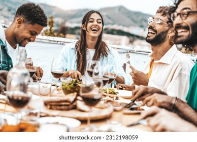 Multiethnic friends having fun at rooftop bbq dinner party - Group of young people diner together sitting at restaurant dining table - Cheerful multiracial teens eating food and drinking wine outside - Powered by Shutterstock