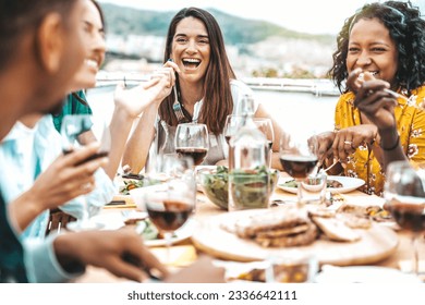 Multiethnic friends having fun at rooftop bbq dinner party - Group of young people diner together sitting at restaurant dining table - Cheerful multiracial teens eating food and drinking wine outside - Powered by Shutterstock