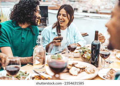 Multiethnic friends having fun at rooftop bbq dinner party - Group of young people diner together sitting at restaurant dining table - Cheerful multiracial teens eating food and drinking wine outside - Powered by Shutterstock