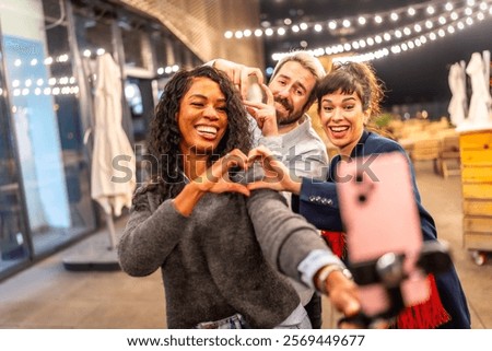 Multi-ethnic friends join hands gesturing heart shape while vlogging online in a night party