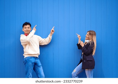 Multi-ethnic friends pointing at something while standing in front of a sheet metal wall.
