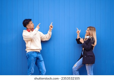 Multi-ethnic friends pointing at something while standing in front of a sheet metal wall.