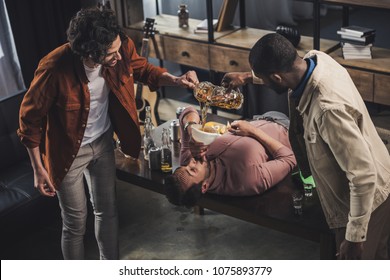 Multiethnic Friends Pouring Beer In Funnel And Man Drinking While Lying On Table