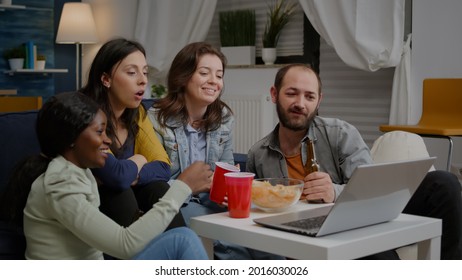 Multiethnic Friends Sitting On Couch Having Online Videocall Meeting Socialising With Virtual Collegue Using Laptop. Group Of Mixed Race People Having Fun Together Late At Night In Living Room