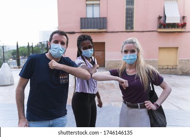 Multiethnic Friends Smiling Looking At Camera Wearing Protective Medical Masks And Waving Their Elbow For Prevention And Not Spreading The Virus. Happy To See Each Other Again. Security Concept