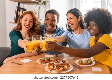 Multi-ethnic friends toasting over breakfast with orange juice and muffins at home - Powered by Shutterstock