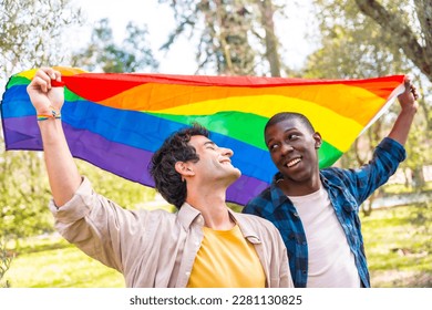 Multi-ethnic gay male couple holding a rainbow lgbt symbol flag, smiling - Powered by Shutterstock