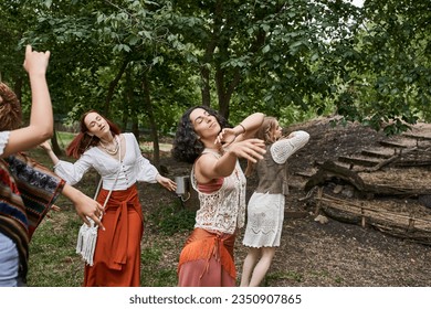 multiethnic girlfriends in stylish clothes dancing with closed eyes in outdoor retreat center