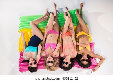 multiethnic girls in swimsuits and sunglasses sunbathing on swimming mattresses