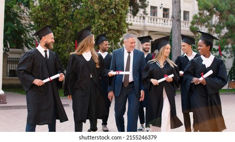 Multiethnic Graduates Students In The College Park Walking In Group With The College Principal After The Graduation Very Exciting Holding Diplomas And Discussing All Together