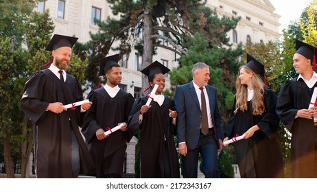 Multiethnic Graduates Students In The College Park Walking In Group With The College Principal After The Graduation Very Exciting Holding Diplomas And Discussing All Together