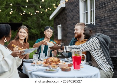 Multiethnic group of adult friends enjoying dinner party outdoors sitting at dining table together and sharing delicious homemade meal - Powered by Shutterstock