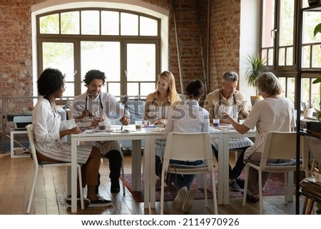 Multiethnic group of art school students of young and mature ages enjoying artistic hobby together, studying drawing on art school studio class, painting at table, chatting, laughing