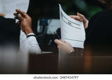 Multiethnic group of business people collaboratively working on a project, seated in a comfortable restaurant setting with papers and digital devices. - Powered by Shutterstock