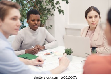 Multi-ethnic Group Of Business People Discussing Project While Working Sitting At Meeting Table, Focus On African-American Man Listening Intently To Partners