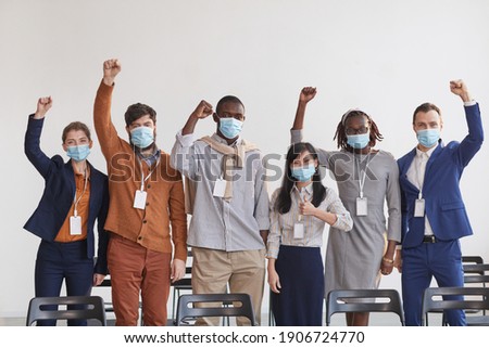 Multi-ethnic group of business people wearing masks and cheering while standing in row against white in conference room