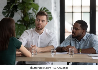 Multi-ethnic group of businesspeople sit at table negotiating during meeting in office board room, client and executives communication. HR manager and unconvincing applicant at job interview concept
