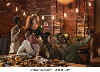 Multi-ethnic group of cheerful adult people taking selfie photo while enjoying party with outdoor lighting
