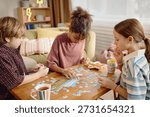 Multiethnic group of children assembling jigsaw puzzle on wooden table, Caucasian boy, Black girl, Caucasian girl focusing on pieces, drinks and snacks nearby, casual indoor setting