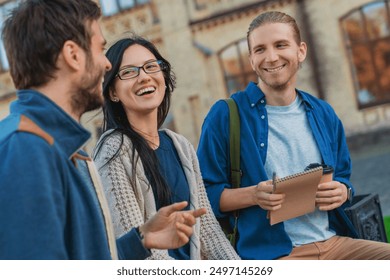 Multi-ethnic group of college students friends classmates in casual clothing sitting outside in university campus laughing and having fun talking with each other resting while education study break. - Powered by Shutterstock