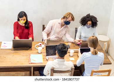 Multiethnic Group Of Co-workers At Work In A Temporary Office, Protective Face Masks Worn, Plexiglass Barrier To Protect Health, The New Normal Concept Applied To Smart Business