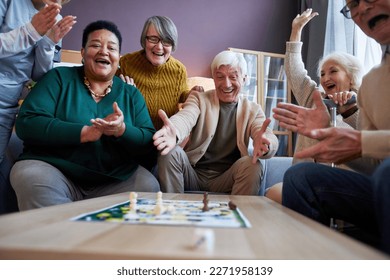 Multiethnic group of excited senior people playing board games at retirement home and celebrating win - Powered by Shutterstock