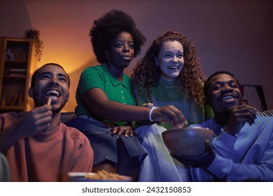 Multiethnic group of excited young people watching comedy movie together in dark room - Powered by Shutterstock