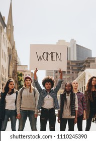 Multi-ethnic Group Of Females Protesting For Women Empowerment Outdoors On Road. Young African Female With Group Holding Banner Sign During A Protest.