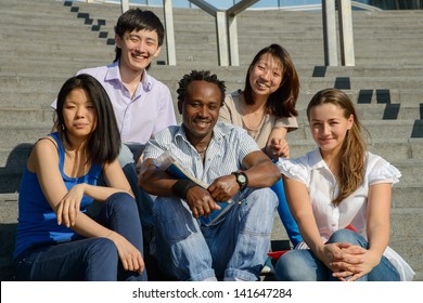 Multiethnic Group Of Five University Students Sitting On Steps Of University Smiling, Metaphor For Diversity And International Friendship