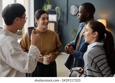 Multiethnic group of four cheerful adults as colleagues chatting and enjoying coffee break in office - Powered by Shutterstock