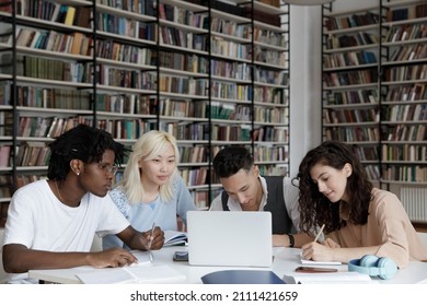 Multiethnic Group Of Four Gen Z University Students Working Together At Laptop, Writing Notes, Watching Learning Webinar, Online Lecture, Reading Tutorials On Internet In College Library