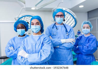multi-ethnic group of four healthcare workers, a team of doctors, surgeons and nurses, performing surgery on a patient in a hospital operating room. They are looking at the camera.