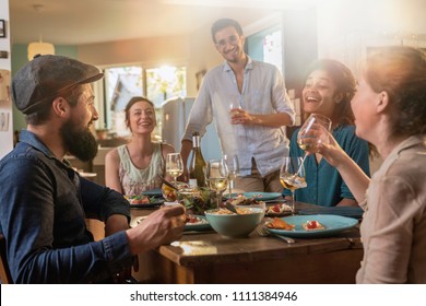 Multi-ethnic group of friends having fun while sharing a meal in a warm and welcoming house. They discuss , while the sun comes in through the window