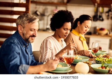 Multi-ethnic Group Of Friends Having Lunch At Dining Table. Focus Is On Black Woman Eating Pasta. 