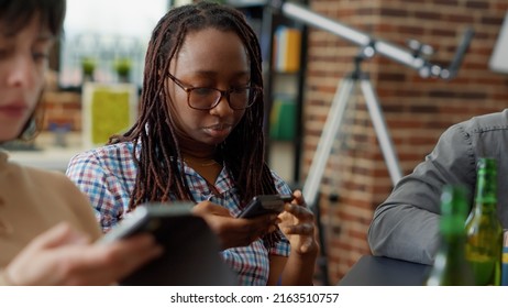 Multiethnic Group Of Friends Sitting Together And Using Smartphone, Not Talking And Scrolling Through Social Media App. People Looking At Mobile Phone Screen. Handheld Shot. Close Up.